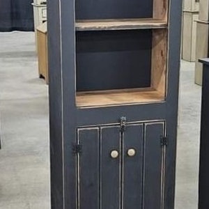 May include: A tall, dark blue cabinet with a distressed finish. The cabinet has a glass-fronted upper section with two shelves and a lower section with two doors. The doors have vertical paneling and round, light-coloured knobs. The cabinet is made of wood.