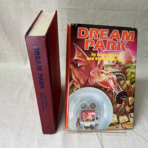 May include: Two paperback books with red covers. The book on the left has the title "DREAM PARK" in blue lettering. The book on the right has the title "DREAM PARK" in white lettering with a colorful illustration of a dragon.