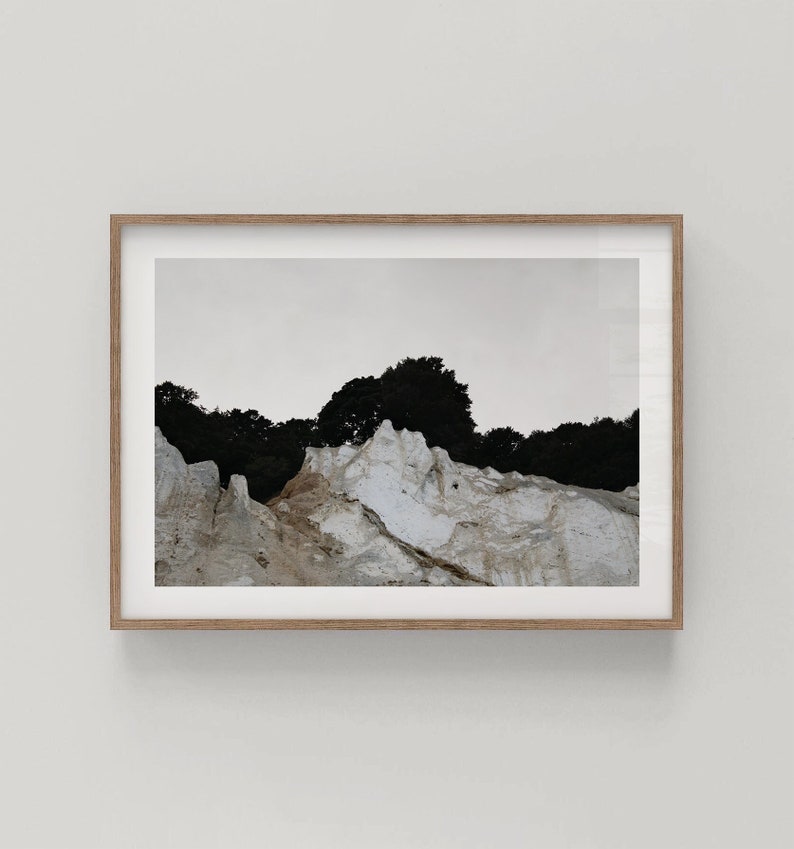 Peut inclure: Une photographie en noir et blanc d'une falaise rocheuse avec une ligne d'arbres au sommet. La falaise est principalement blanche avec des zones brunes et grises.