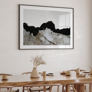 Peut inclure: Une table &agrave; manger en bois avec six chaises, un vase avec des fleurs s&eacute;ch&eacute;es, un livre et quelques tasses et soucoupes. Une photographie encadr&eacute;e d'un paysage rocheux avec des arbres est accroch&eacute;e au mur derri&egrave;re la table.