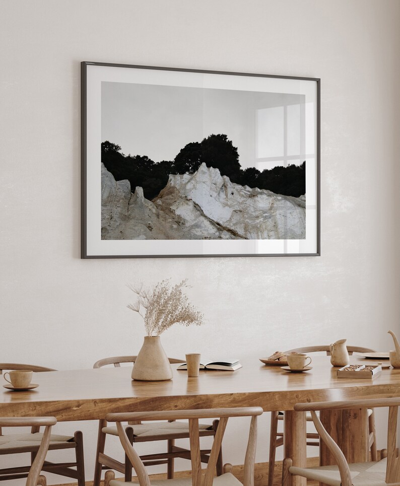 Peut inclure: Une table &agrave; manger en bois avec six chaises, un vase avec des fleurs s&eacute;ch&eacute;es, un livre et quelques tasses et soucoupes. Une photographie encadr&eacute;e d'un paysage rocheux avec des arbres est accroch&eacute;e au mur derri&egrave;re la table.