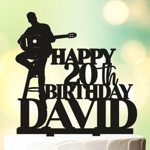 May include: Black silhouette cake topper of a person playing a guitar with the text "Happy 20th Birthday David" on a white cake.