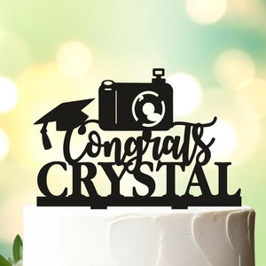 May include: Black silhouette of a camera, graduation cap, and the text "Congrats Crystal" on a white cake.