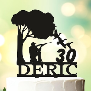 May include: Black silhouette cake topper of a hunter with a gun, two birds flying away, a tree, and the name "DERIC" and the number "30" on a white cake.