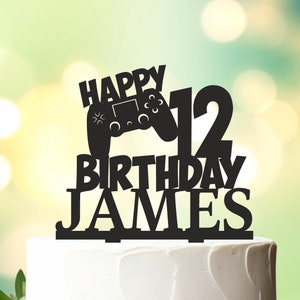 May include: Black and white cake topper with a video game controller, the number 12, and the words "Happy Birthday James".
