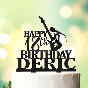 May include: Black acrylic cake topper with a guitar and microphone, the text "Happy 18th Birthday Deric" and the design number "Design 65/2".