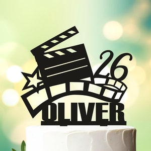 May include: Black cake topper with a film reel, clapperboard, star and the number 26. The name Oliver is written below the design.  Design 3811.