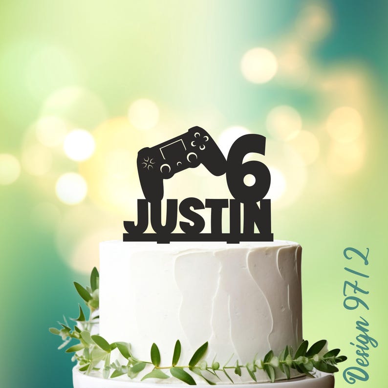 May include: Black cake topper with a video game controller and the number 6, along with the name Justin.