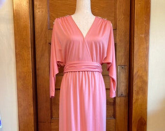 May include: A long, pink maxi dress with a V-neckline and a wrap-style bodice. The dress has long sleeves and a sash that ties at the waist.