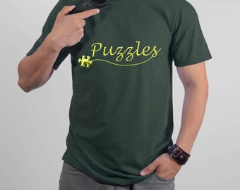Puede incluir: Una camiseta verde oscuro con la palabra "Puzzles" escrita en cursiva amarilla. Una pieza de rompecabezas amarilla está a la izquierda de la palabra.