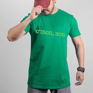May include: A green t-shirt with a pineapple graphic and the text "c'mon, son" in yellow.