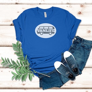 A blue t-shirt lays flat. The shirt has a white circular embellishment featuring a graphic of a van that reads VAN LIFE