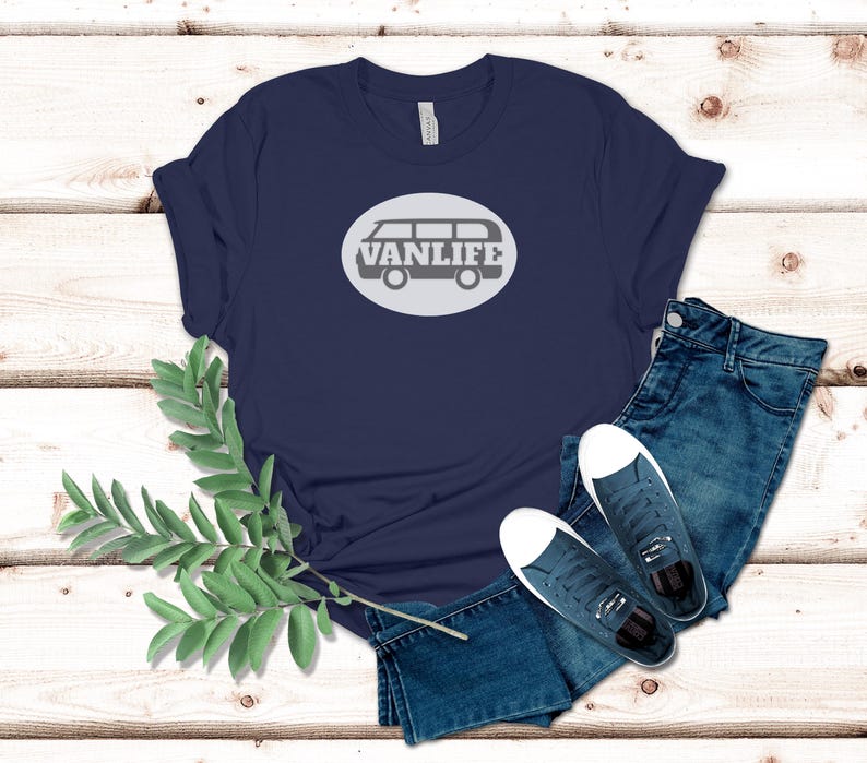 A navy blue t-shirt lays flat. The shirt has a white circular embellishment featuring a graphic of a van that reads VAN LIFE