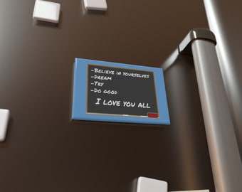 May include: A blue chalkboard with a white frame and the text "Believe in yourselves, Dream, Try, Do good, I love you all" written on it. The chalkboard is attached to a stainless steel refrigerator with a white magnet.