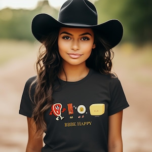 May include: Black t-shirt with a graphic of cartoon food characters, including a steak, bacon, egg, and butter. The text "BBBE HAPPY" is printed below the graphic.