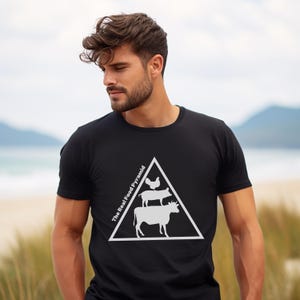 May include: Black t-shirt featuring a white graphic of a food pyramid with a cow, pig, and chicken. The text "The Real Food Pyramid" is printed on the left side of the triangle. The shirt is made of a soft material.