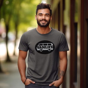 A man in a dark grey t-shirt with a black embellishment featuring a graphic of a van that reads VAN LIFE