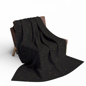 May include: A black throw blanket with a pattern of small, golden-yellow dots is draped over a brown chair. The blanket is soft and appears to be made of a comfortable material. The chair has a wooden frame.