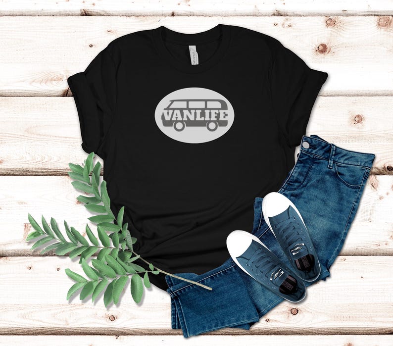 A black t-shirt lays flat. The shirt has a white circular embellishment featuring a graphic of a van that reads VAN LIFE