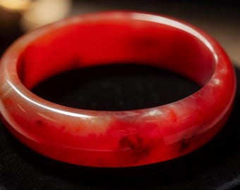 May include: A red carnelian bangle bracelet with a polished finish. The bracelet is made of natural stone and has a unique marbled pattern.