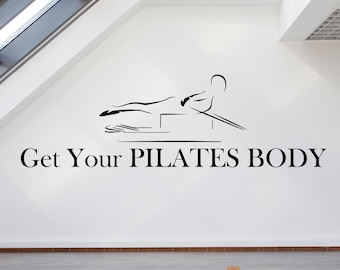 May include: A white room with a skylight and a blue yoga mat on the floor. The wall has a black and white illustration of a person doing pilates and the text "Get Your PILATES BODY".