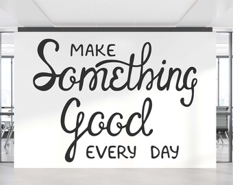 May include: A white wall with black lettering that reads "Make Something Good Every Day" in a modern calligraphy style. The wall is in an office setting with glass walls and modern furniture.
