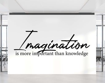 May include: A white wall with black lettering that reads "Imagination is more important than knowledge". The wall is in an office setting with glass walls and black office chairs.