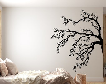 Könnte beinhalten: Ein Schlafzimmer-Interieur mit einer weißen Wand, auf der eine schwarze Silhouette eines Baumzweigs mit Blättern zu sehen ist. Das Bett ist mit einer weißen und beigefarbenen Decke und Kissen bezogen. Ein kleiner Holz-Beistelltisch mit einer Lampe steht neben dem Bett.
