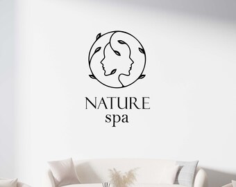 May include: A white room with a white couch and two white armchairs. A gold and glass coffee table sits in front of the couch. The wall behind the furniture has a black and white logo that reads "NATURE spa" with a stylized image of two faces intertwined with leaves.