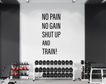 以下が含まれることがあります： 黒い文字で「NO PAIN NO GAIN SHUT UP AND TRAIN！」というモチベーションを高める言葉が書かれた白い壁。壁は、黒と白のウェイトラックと黒いウェイトベンチのあるジムにある。