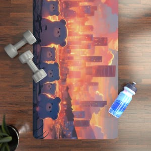 May include: A yoga mat with a cityscape design and cartoon bears. Two gray dumbbells and a blue water bottle are on a wooden surface. The mat features a sunset-colored sky and buildings.