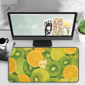 May include: A computer desk mat featuring a vibrant design of sliced kiwis, oranges, and lemons. A small, cartoon cat peeks out from behind the fruit. The computer monitor displays the text "Welcome to Adorable S2".