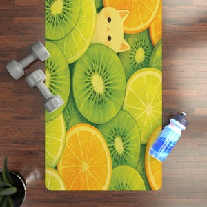 May include: A yoga mat with a vibrant fruit pattern of kiwi, lemon, and orange slices, with a cartoon cat peeking out. Gray dumbbells and a blue water bottle are on the wooden floor.