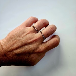 May include: Two thin, braided copper rings on a hand. The rings are a simple, minimalist design.