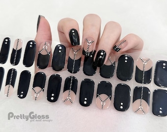 May include: Black and nude gel nail wraps with various designs. Some wraps feature a half-and-half design with a line of small silver dots. Others have a black base with a nude accent and silver embellishments. The text "Pretty Gloss gel nail wraps" is visible.