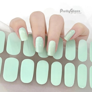 May include: A sheet of light green gel nail wraps with a hand model wearing the wraps on their fingernails. The sheet has 20 individual wraps, each shaped like a rounded rectangle. The brand name "PrettyGloss gel nail wraps" is printed in the top right corner of the image.