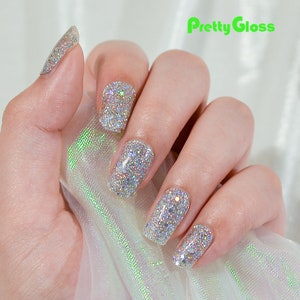 May include: Close-up of a hand with silver glitter nail polish. The nails are short and square shaped. The glitter is iridescent and catches the light. The hand is holding a piece of sheer fabric.