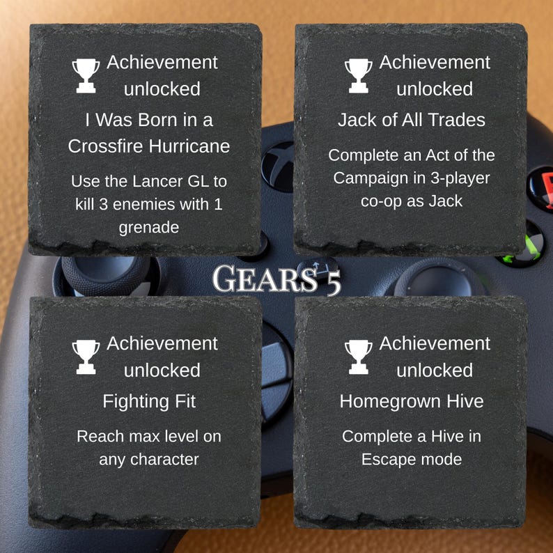 Puede incluir: Cuatro posavasos cuadrados de pizarra con texto blanco y gr&aacute;ficos de trofeos. Cada posavasos muestra un mensaje de "Logro desbloqueado" y un desaf&iacute;o espec&iacute;fico del juego Gears 5. El logotipo del juego est&aacute; en el centro.