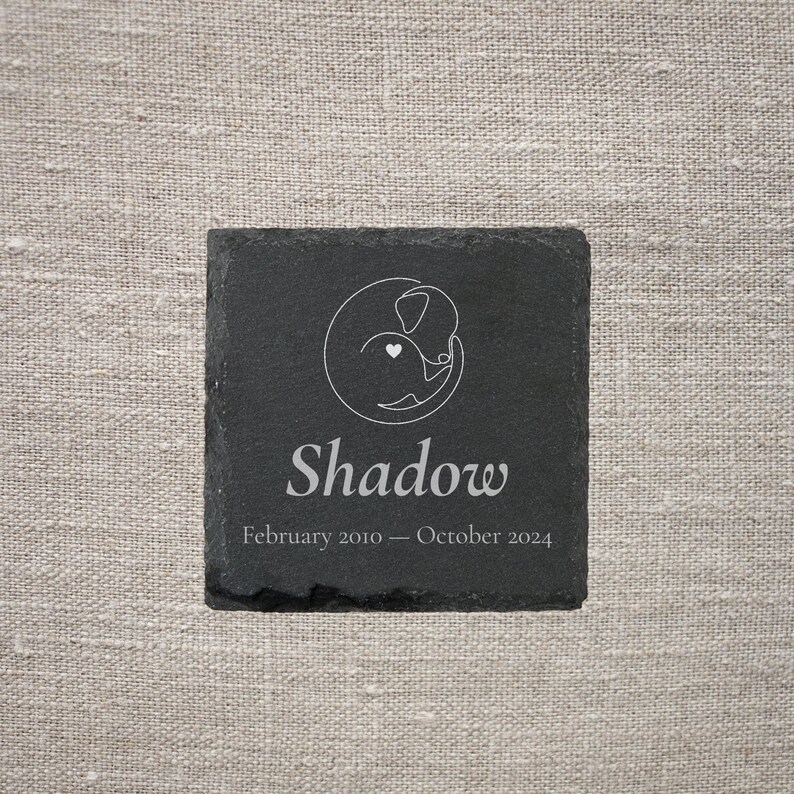 Pode incluir: Uma base para copos quadrada de ard&oacute;sia preta com um desenho a tra&ccedil;o branco de um c&atilde;o e um cora&ccedil;&atilde;o. O nome "Shadow" est&aacute; abaixo do desenho, com as datas "Fevereiro 2010 - Outubro 2024".