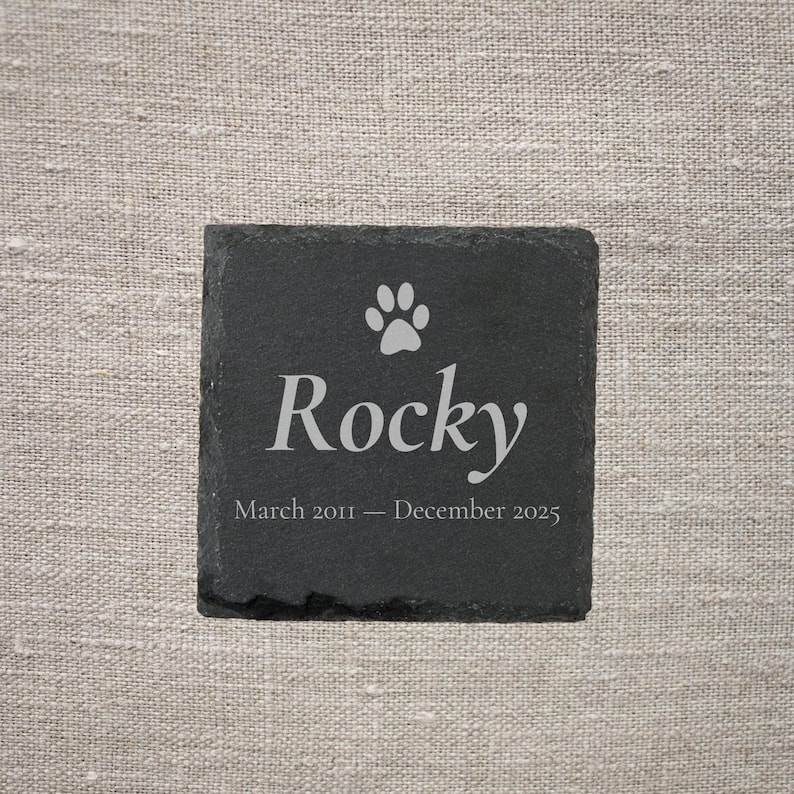 Pode incluir: Base quadrada de ard&oacute;sia preta com uma pegada e o nome "Rocky" em branco. O texto "Mar&ccedil;o 2011 - Dezembro 2025" est&aacute; abaixo. Um item de mem&oacute;ria.