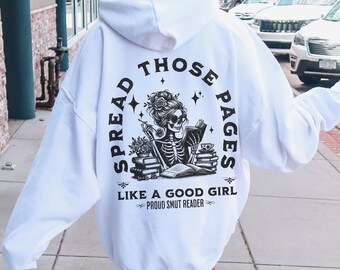 May include: White hoodie with a black and white graphic print of a skeleton reading a book. The graphic says "Spread Those Pages Like A Good Girl - Proud Smut Reader -"