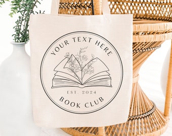Puede incluir: Una bolsa de lona beige con un logotipo circular negro que presenta un libro abierto con flores y el texto "YOUR TEXT HERE EST. 2024 BOOK CLUB".