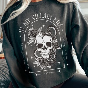 May include: A dark gray sweatshirt with a skull and snake graphic and the text "In My Villain Era".
