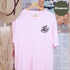 May include: Pink t-shirt featuring a black graphic of a hand reaching for a book with the text "Dark Romance Club".