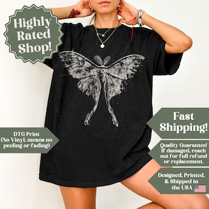 Puede incluir: Una camiseta negra de manga corta con un gran gr&aacute;fico blanco desgastado de una polilla con alas largas y extendidas centrado en el pecho. El dise&ntilde;o tiene una apariencia texturizada y envejecida, y la camiseta tiene un corte holgado.