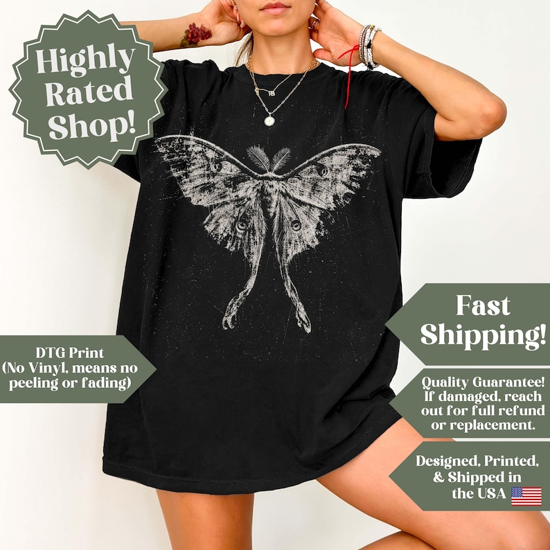 Puede incluir: Una camiseta negra de manga corta con un gran gr&aacute;fico blanco desgastado de una polilla con alas largas y extendidas centrado en el pecho. El dise&ntilde;o tiene una apariencia texturizada y envejecida, y la camiseta tiene un corte holgado.