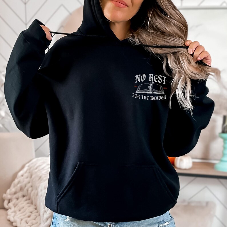 Peut inclure: Sweat &agrave; capuche noir avec une poche avant et un cordon de serrage. Le haut de la poitrine porte l'inscription "NO REST" au-dessus d'un dessin de livre ouvert, avec "FOR THE READER" en dessous. Le design est de style vintage et gothique.