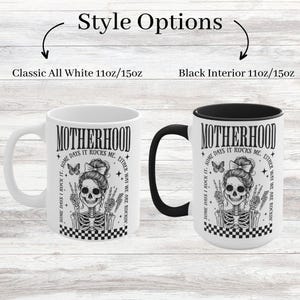 May include: White ceramic mug with a black interior and a black and white graphic of a skeleton with the text "Motherhood Some Days I Rock It. Some Days It Rocks Me. Either Way We Are Rockin'" printed on it. The mug is available in two sizes: 11oz and 15oz.