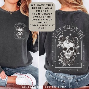 May include: A black sweatshirt with a skull and snake design on the back. The design is surrounded by flowers and stars. The text "In My Villain Era" is written in a gothic font above the skull. The sweatshirt also has a pocket on the front with the same design in a smaller size.