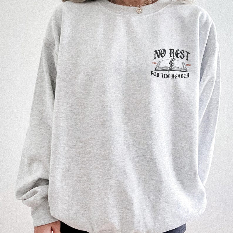 Peut inclure: Un sweat-shirt gris clair avec l'inscription noire "NO REST FOR THE READER" au-dessus d'un dessin de livre ouvert. Le sweat-shirt est de style col rond et semble &ecirc;tre fait d'une mati&egrave;re douce.